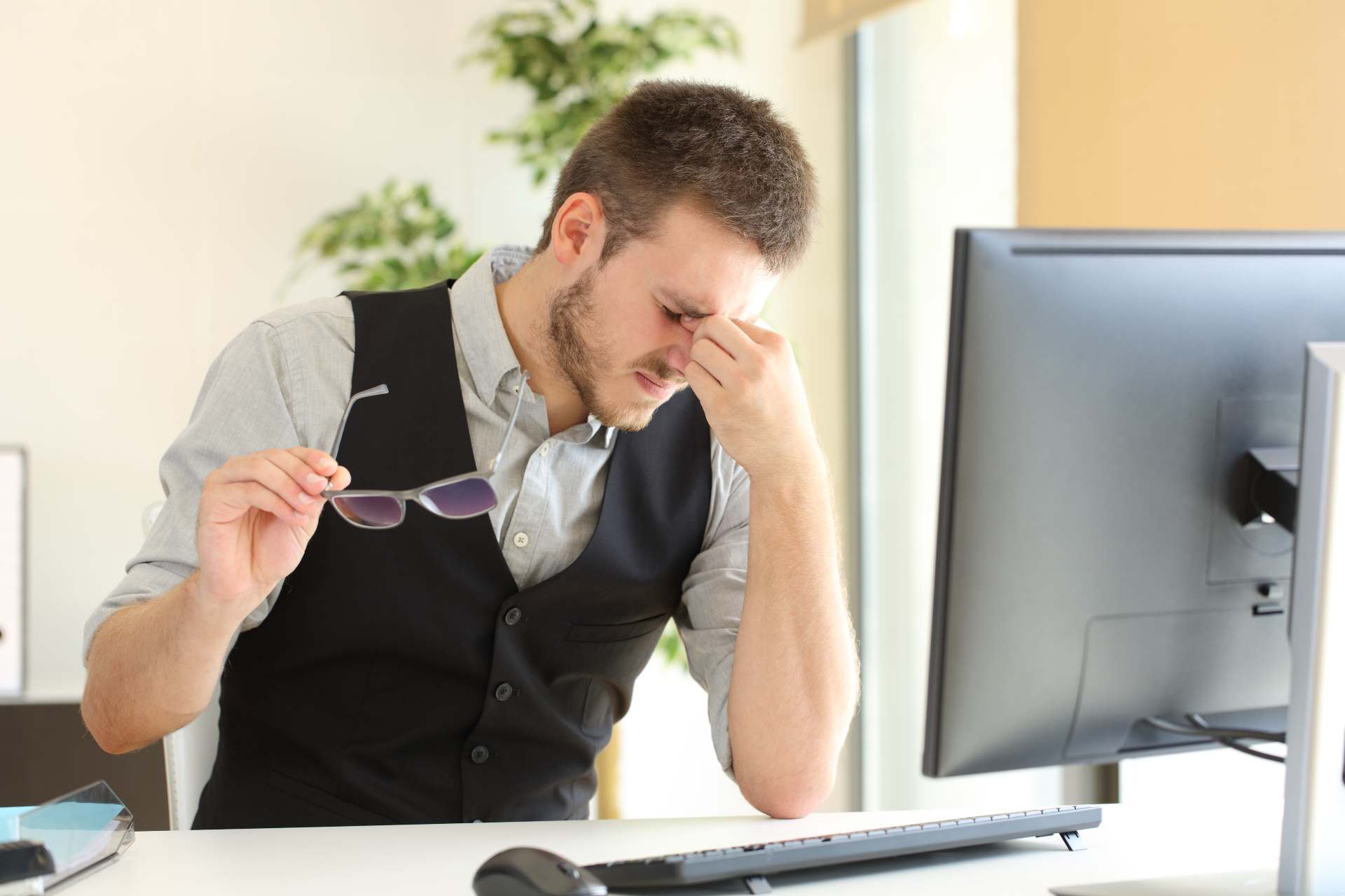 a man suffering from digital eye strain headaches looking at his office computer screen 
