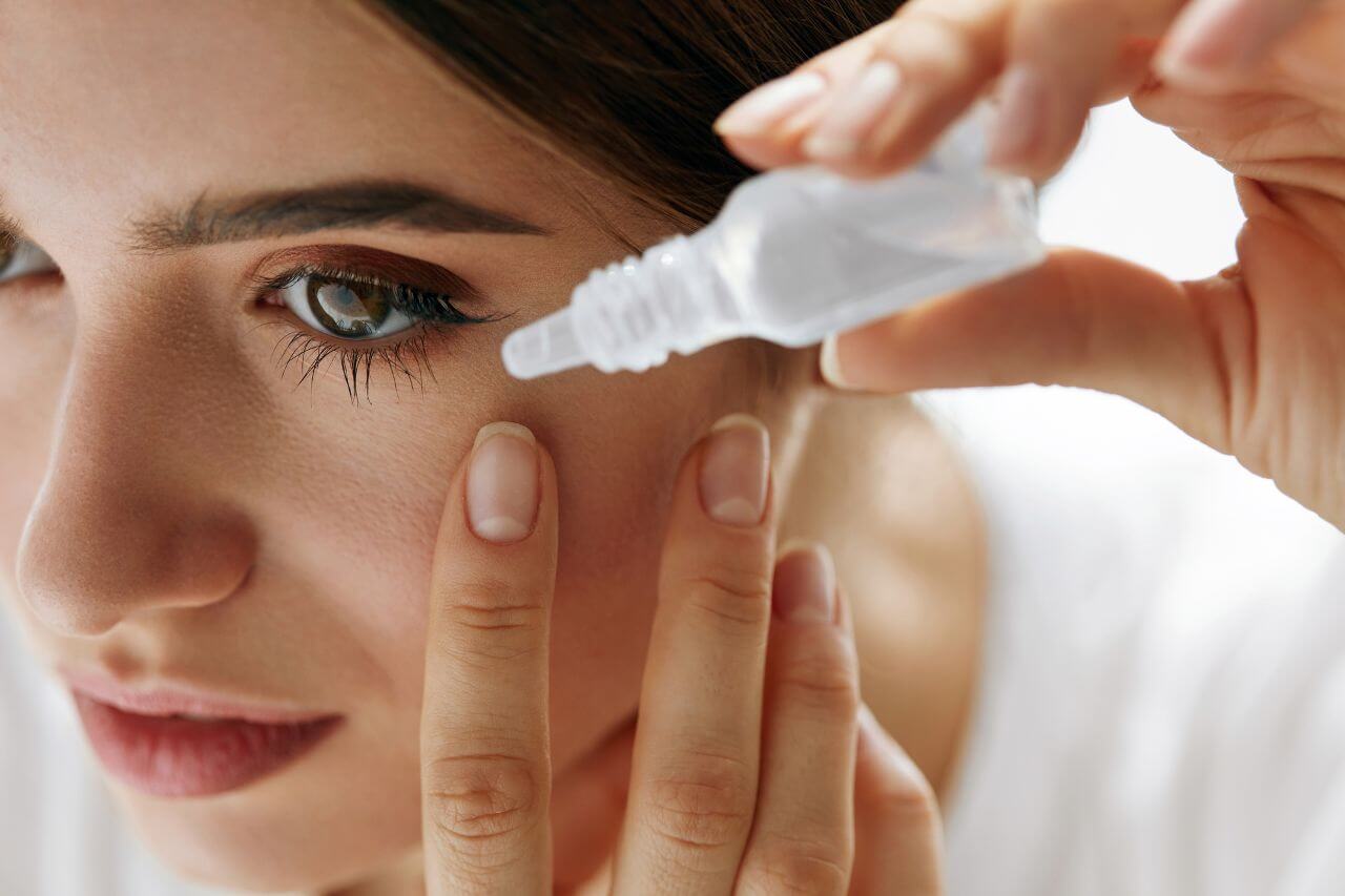 Young woman pouring eye drops into her left eye
