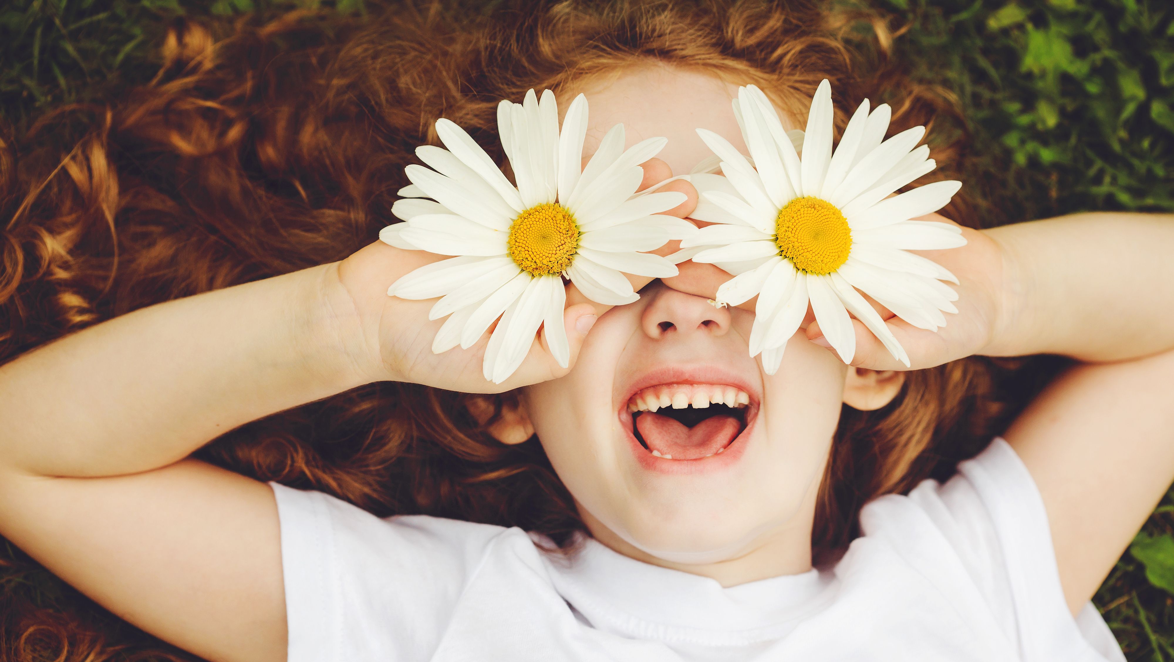 a young girl laughing and playing outside in the summer with daisies over her eyes